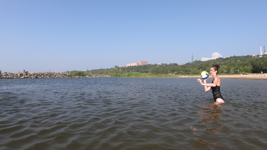 A beautiful girl and a middle-aged man playing ball on the river during the summer holiday. Entertainment on the water during the holidays