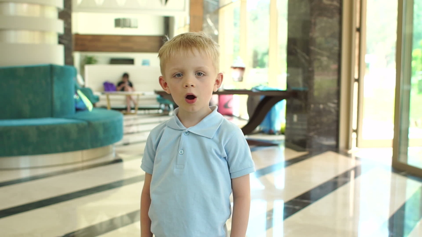 Funny little boy of 5 years old having fun and dancing in the lobby of the hotel. Child playing and dancing funny dance and smiling in the room with beautiful interior, slow motion.