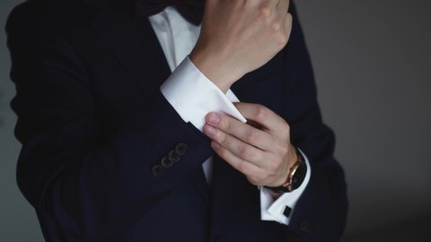 Stylish young man in blue suit adjusts his cufflinks of white shirt. Close-up. Interior. Sunshine. Steady