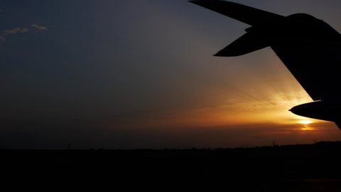 Panning shot of a airplane tale silhouette with the sunset over the horizon.