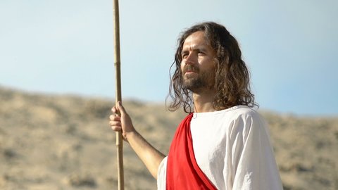 Jesus with stuff in robe looking at desert and smiling after long road, close-up