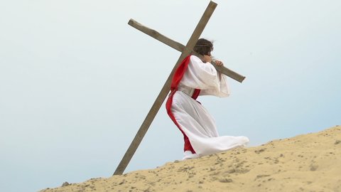 Exhausted Jesus carrying heavy wooden cross walking to Calvary hill, crucifixion