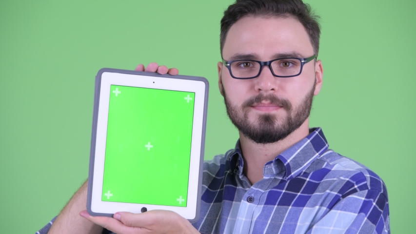 Face of happy young bearded hipster man showing digital tablet