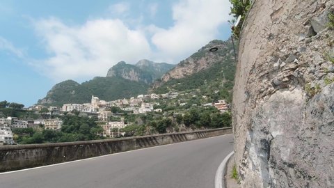 Positano, Italy, August 2019: POV dash camera tracking shot front view of driving in the mountainous curvy narrow road of Amalfi coast getting close to Positano town in Italy