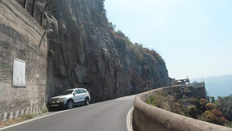 Amalfi, Italy, August 2019: POV dash camera tracking shot front view of driving in the mountainous curvy narrow road of Amalfi coast in Italy
