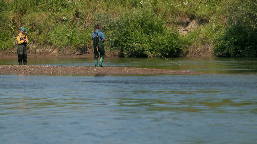 Fishing, two men in special clothes holding fishing rods, throw on floats, fishermen fishing on the river for a small, beautiful nature, Sunny summer day, flying birds, slow motion, Wide angle
