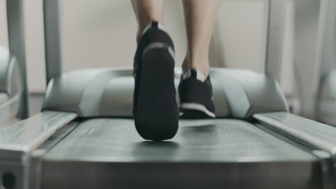 Closeup athletic feet running on treadmill in fitness gym. Back view of black shoes having workout on treadmill. Low view sneakers training in sport club.