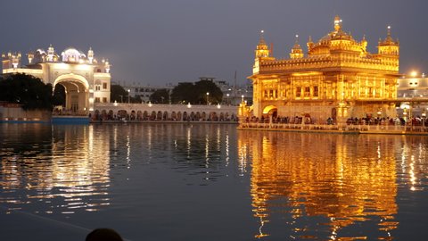 panning shot of the golden temple complex and sacred pool at night in amritsar, india