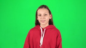 Beautiful girl feeling happy and satisfied showing yeah in the studio on green background. The girl is wearing a red jacket, she has long hair. Slow motion