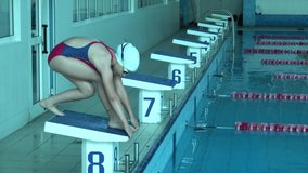 Male swimmer jumps off starting block and start swims in pool HD slow-motion video. Professional athlete training: dive and splashes water surface.