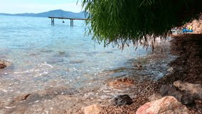Beautiful view of the Ionian sea in Corfu, Greece, stones in the rocky beach, plants in the foreground, a pier in the foreground. 4K UHD video.