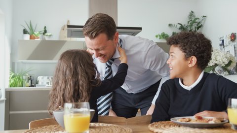 Daughter Helping Businessman Father To Put On Tie As Children Eat Breakfast In Kitchen Before School