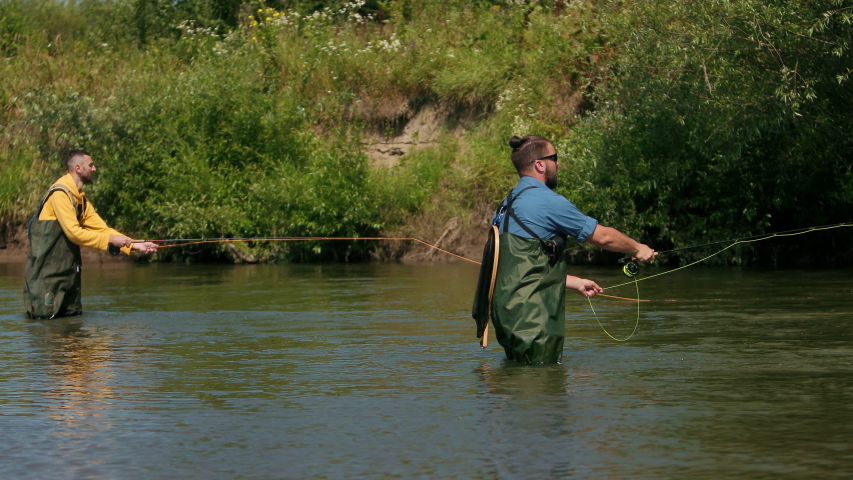 angling, two men in special clothes holding fishing rods, throw on floats, fishermen fishing on the river for a small, beautiful nature, Sunny summer day, flying birds, slow motion, Wide angle