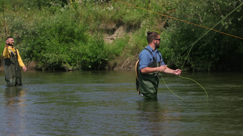 Fishing, two men in special clothes holding fishing rods, throw on floats, fishermen fishing on the river for a small, beautiful nature, Sunny summer day, flying birds, slow motion, Wide angle