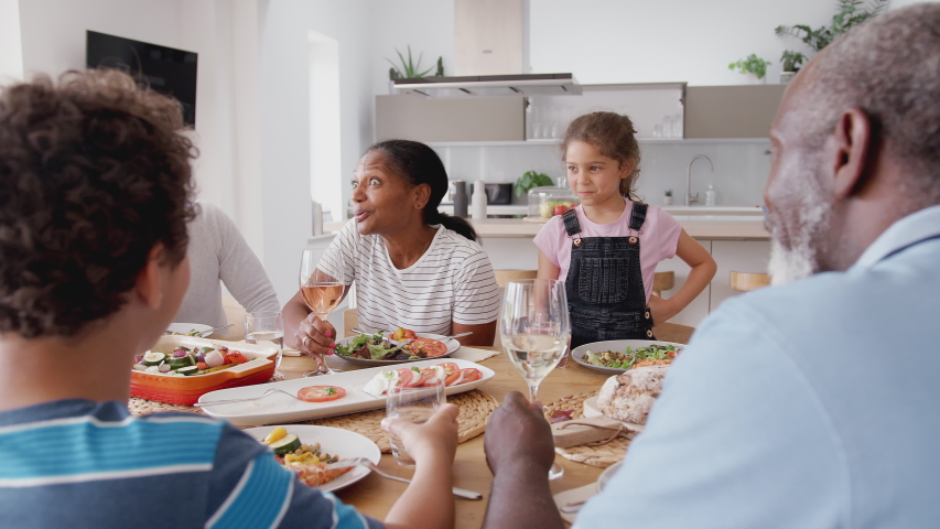 Multi-Generation Mixed Race Family Making A Toast Before Eating Meal Around Table At Home Together