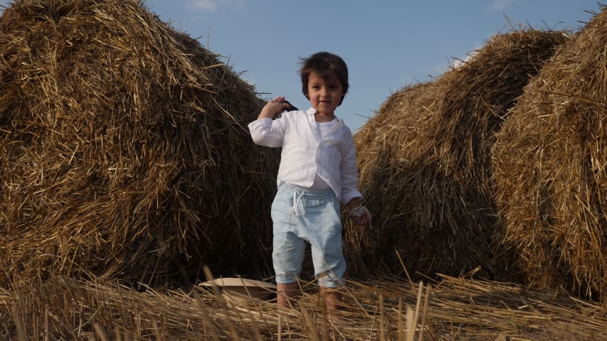 boy in white shirt and t-shirt in blue pants dancing in the field next to a haystack at sunset