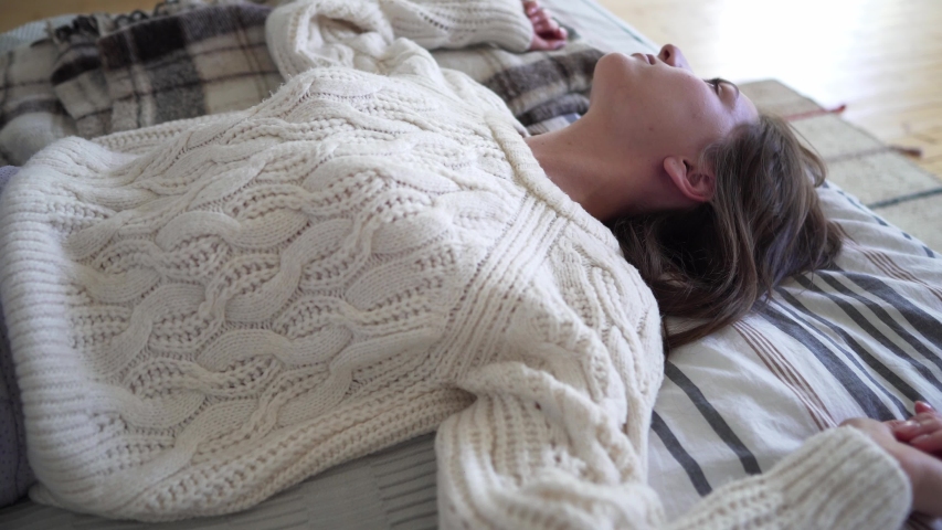 Happy Caucasian young woman basking at home on a cold autumn evening, smiling and looking at the camera. White woolen knitted sweater closeup, hugge concept