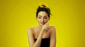 Beautiful girl with sunflowers in her hair sitting in studio on yellow background. Expressive facial features, gentle makeup. Concept for advertising natural cosmetics, skin care, spa treatments.