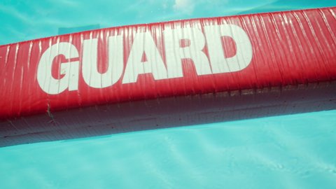 Red lifeguard float on the surface of a public swimming pool. Vibrant life preserver says "guard" in bold letters. The lifeguarding equipment is used in life-saving rescues at water parks. 