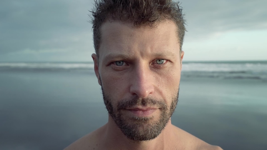 Face of a young handsome unshaven man opens his eyes and looks at the camera on background of the ocean Royalty-Free Stock Footage #1035663944