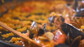 Paella traditional Spanish food. Person putts seafood paella from the fry pan to plate. Paella with with mussels, king prawns, langoustine and squids. Person cooking paella. Dinner. Slow motion 4K