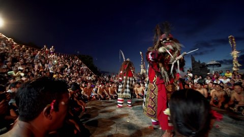 BALI, INDONESIA - JUNE 10, 2019: Outdoor theater full of viewers and stage with actors in masks performing traditional Kecak dance. White beast on the stage. Uluwatu temple, evening