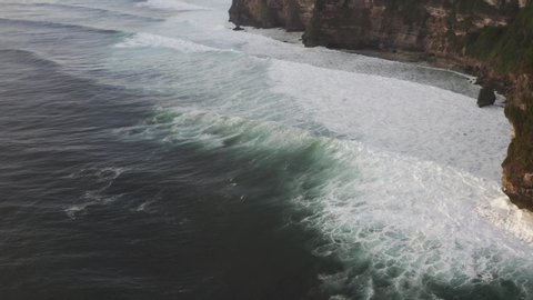 Aerial view of ocean waves splashing near high cliffs with white foam. Bali island, Indonesia