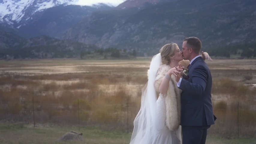 An elegant newly married couple kiss and embrace in a mountain field