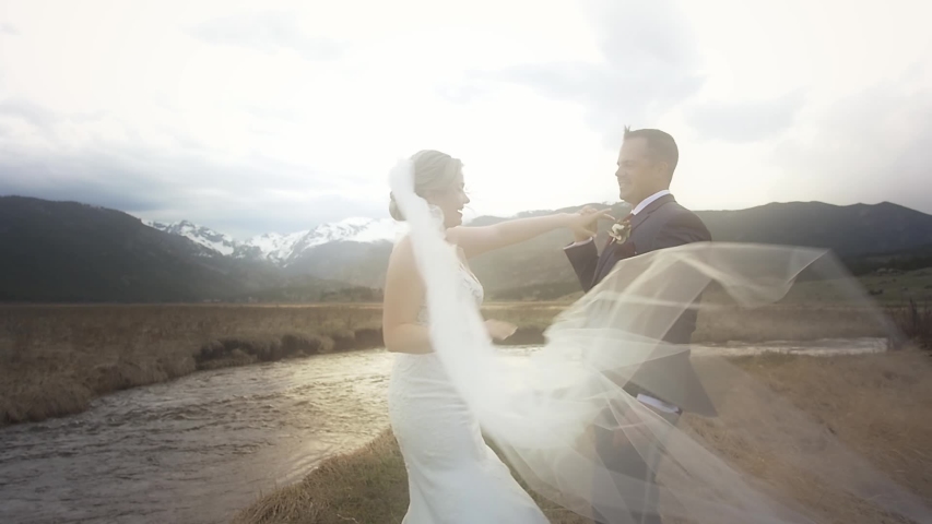 A bride's long veil blows in the wind and across the frame as her groom spins her around for their first dance