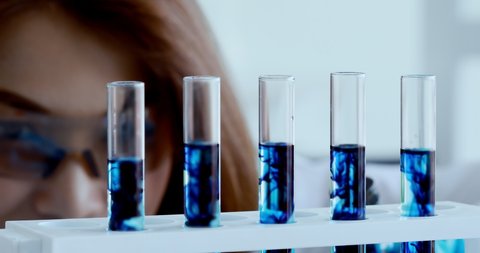 Close up scene video of beautiful Asian female scientist doing experiment in laboratory, she dropping blue liquid into test tube.
