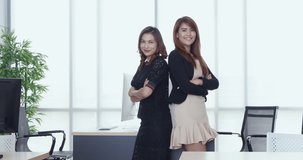Zoom in scene video of smiling beautiful Asian businesswomen standing back to back and crossed their arms in modern office.
