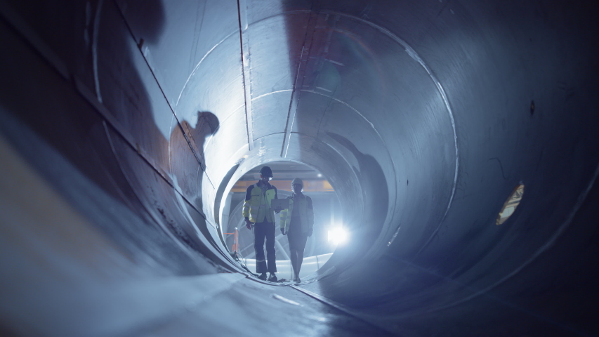 Two Heavy Industry Engineers Walking Inside Pipe, Use Laptop, Have Discussion, Checking Welding. Construction of the Oil, Natural Gas and fuels Transport Pipeline. Industrial Manufacturing Factory Royalty-Free Stock Footage #1035703955