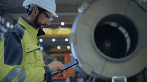 Heavy Industry Engineer Walk Through Pipe Manufacturing Factory, Use Digital Tablet Computer. Facility for Construction of Oil, Gas and Fuel Pipeline Transportation Products. Side View Slow Motion