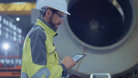 Heavy Industry Engineer Walk Through Pipe Manufacturing Factory, Use Digital Tablet Computer. Facility for Construction of Oil, Gas and Fuel Pipeline Transportation Products. Side View Slow Motion