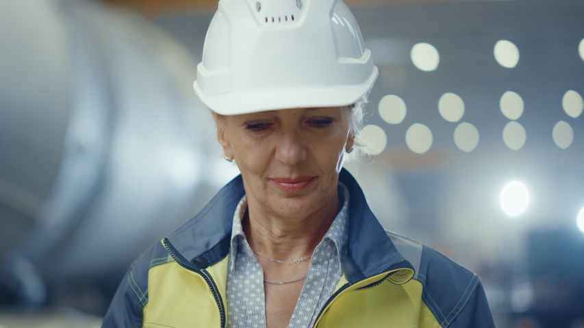 Portrait of Professional Heavy Industry Female Engineer Wearing Safety Uniform and Hard Hat, Smiling Charmingly. In the Background Unfocused Large Industrial Factory where Welding Sparks Flying Royalty-Free Stock Footage #1035704099