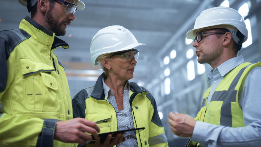 Three Heavy Industry Engineers Stand in Pipe Manufacturing Factory, Use Digital Tablet Computer, Have Discussion. Large Pipe Assembled. Design and Construction of Oil, Gas and Fuels Transport Pipeline Royalty-Free Stock Footage #1035704162