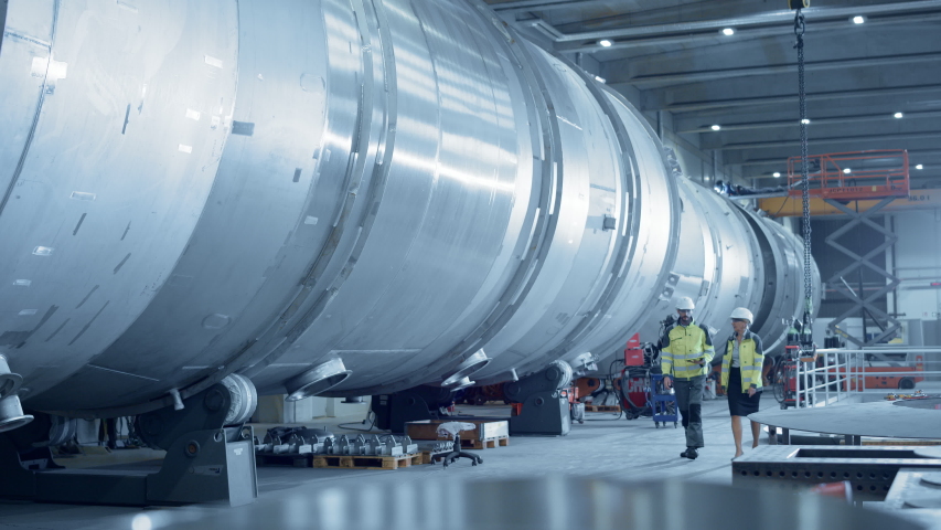Two Heavy Industry Engineers Walking Through Pipe Manufacturing Facility, Use Digital Tablet, Have Discussion. Modern Industrial Design and Construction of Oil, Gas and Fuels Transport Pipeline Royalty-Free Stock Footage #1035704174