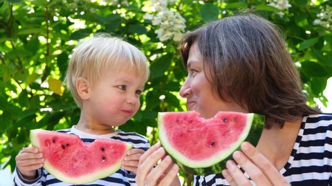 Family picnic, mother and her toddler son eats watermelon on nature green background. Summer food.
