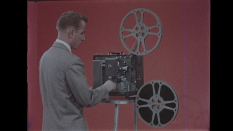 1950s Projectionist Rewinding Film Reel to Reel. 16mm Kodak Pageant Sound Projector. Medium Shot of Man Threading Film. Film Projector Rewinding on Pedestal. Scratched Film, Jump Cut, 4K