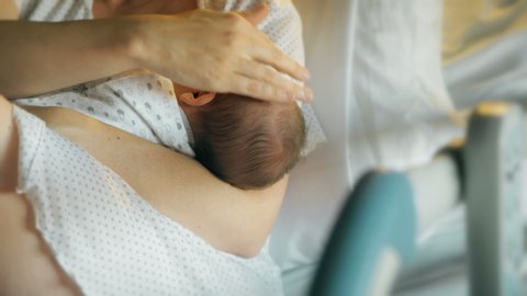 Breastfeeding in the first hours after birth, woman caresses newborn baby. Mother breastfeeds a newborn baby in modern hospital on a medical bed. Emotional moment in beautiful lighting