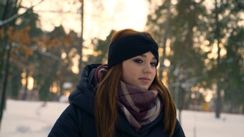 red ginger hair girl walks in a snowy park. Girl drinks coffee from a paper cup. winter evening 4K