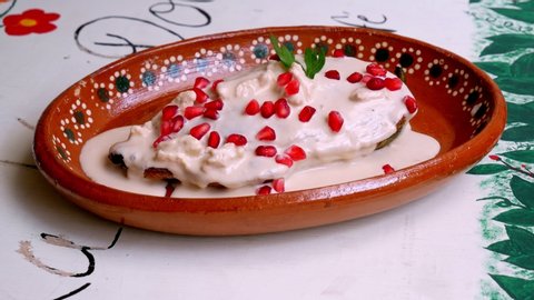 Preparation of the Chile en Nogada, a Mexican cooking recipe with poblano pepper and addition of nogada nuts cream, pomegranate seeds and parsley.