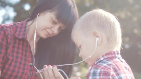 happy family funny slow motion video teamwork outdoors. Mom and son listen to music on a smartphone in the same headphones for two . happy family mother woman and son little lifestyle boy spend time