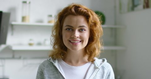 Portrait of young happy woman standing in kitchen, smiling, looking at camera, full of positive emotions, confident in her future, red curly hair, blue eyes, Caucasian. 4K, shot on RED camera.