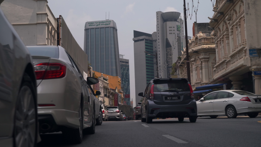 Cars driving-by down city side-street in Kuala Lumpur, Malaysia (ground-level view)