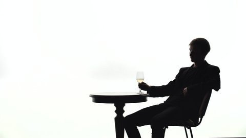 Silhouette of a young confident seducer sitting at a table and raising a glass