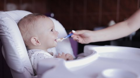 Slow motion, mother feeding puree a baby eating food first time, happy family concept scene