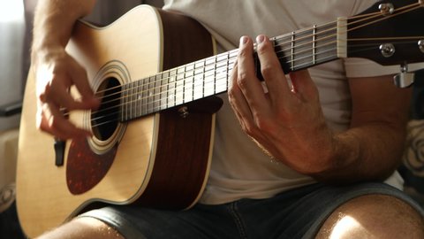 The musician plays a fast rhythm on a yellow acoustic guitar close-up, a ray of light falls on the fingers and neck of the guitar