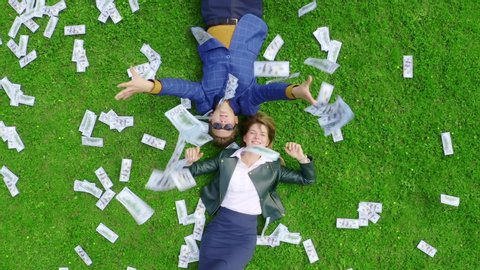 A young man and a girl are lying on a green grassy lawn strewn with money and throwing 100-dollar bills. Jackpot winners concept. Aerial view.