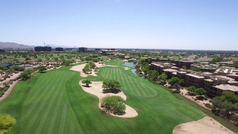 Aerial fly down a golf course's adjacent fairways toward two golf carts in the distance, Scottsdale, Arizona. 